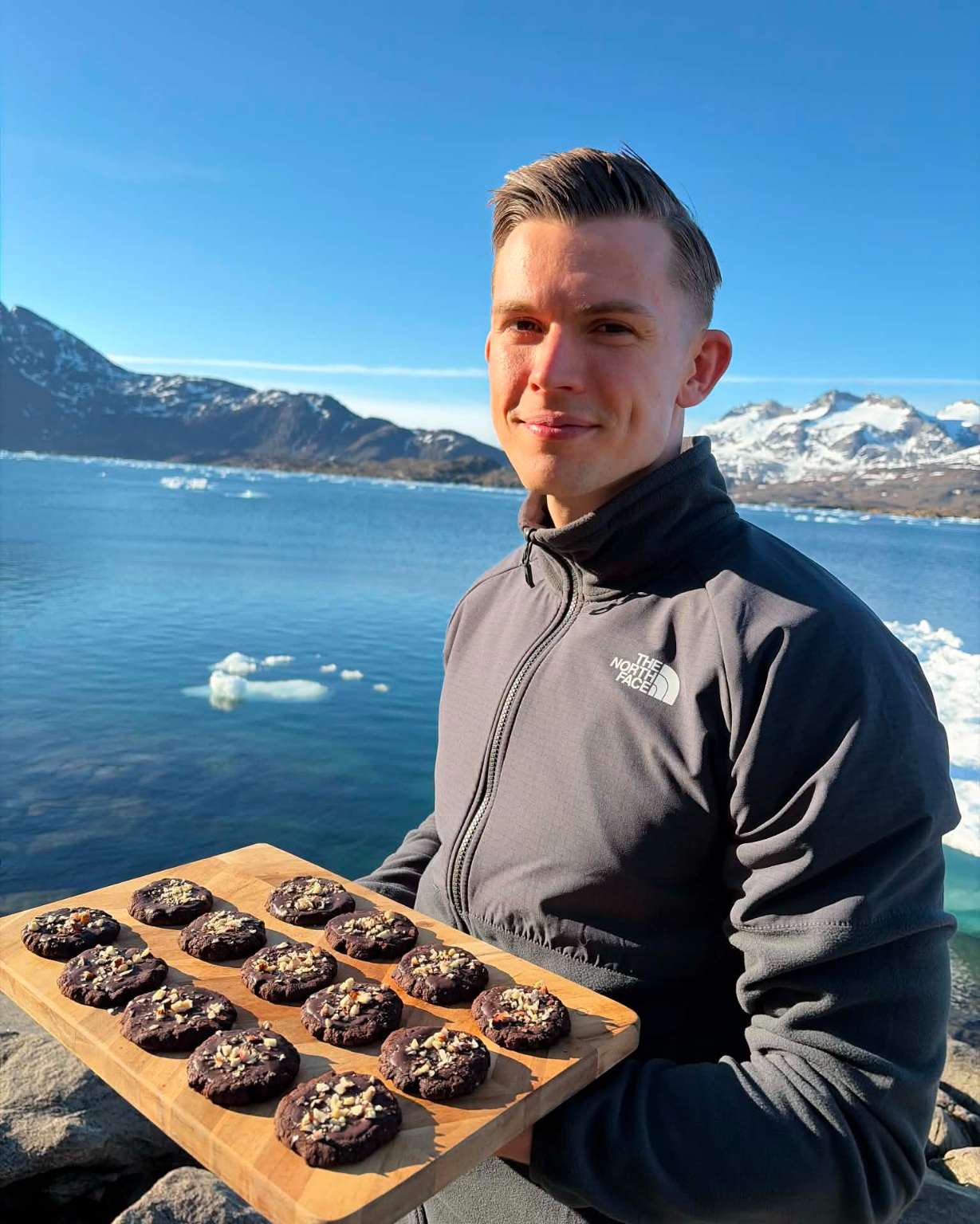 Coachen holder en bakke med hjemmelavede kager ved en fjord.